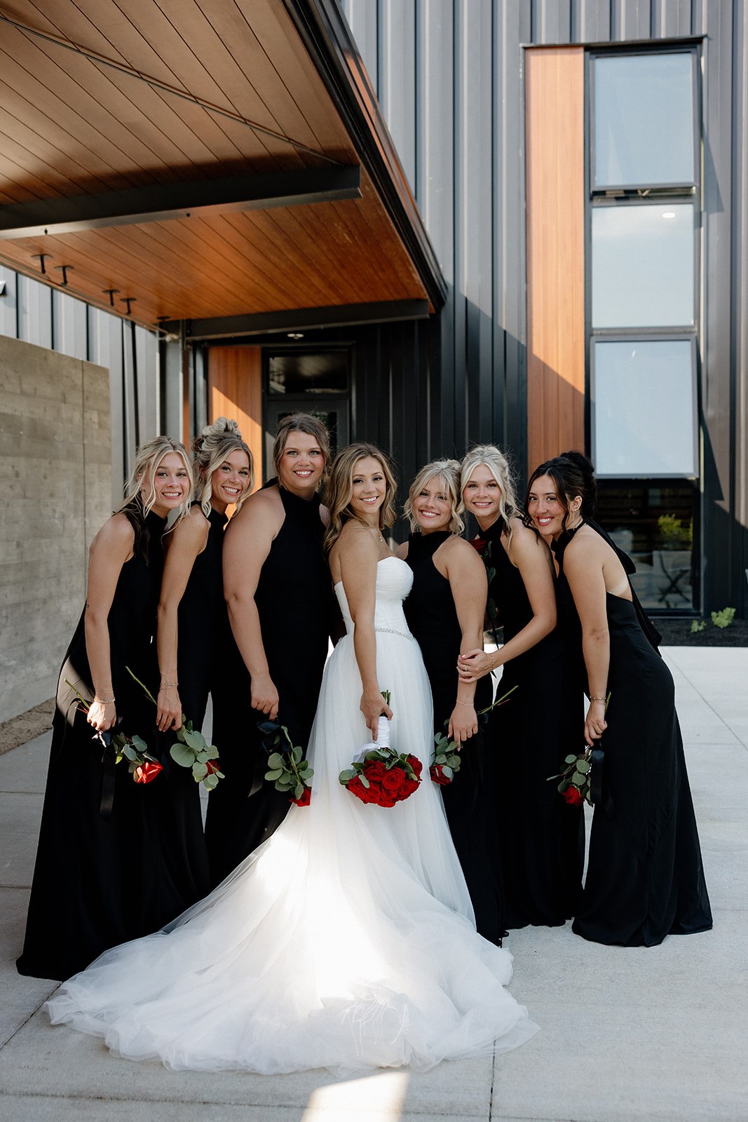 Bride with her bridesmaids holding red roses outside the venue