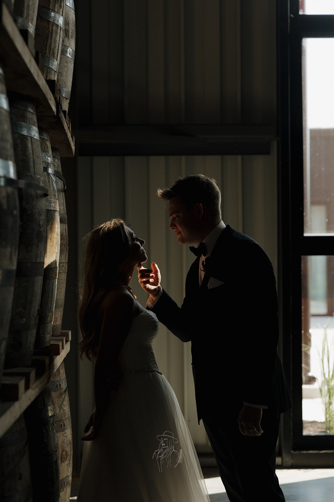Bride and groom silhouetted among bourbon barrels