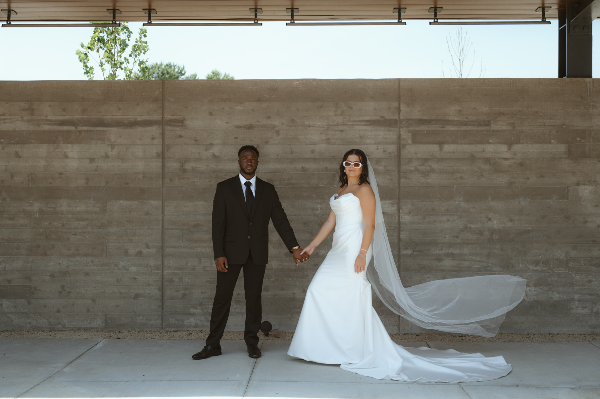 Bride and groom holding hands in front of a concrete wall
