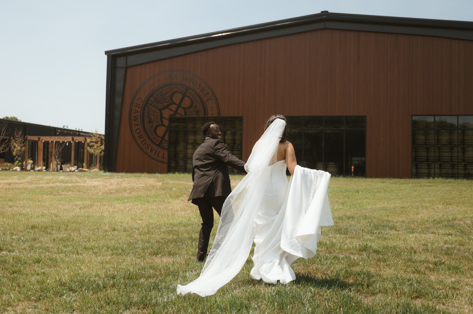 Bride and groom walking together on the lawn in front of the IRA Whiskey distillery building