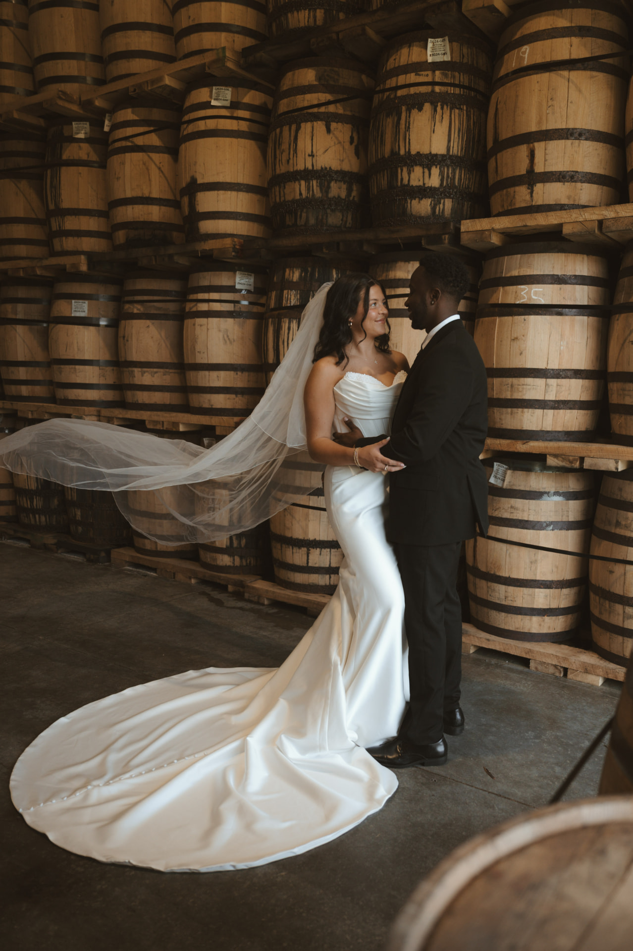 Bride and groom among bourbon barrels in the rack house